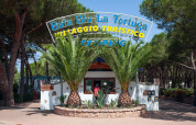 Entrance to Camping Village Baia Blu La Tortuga in Sardinia, Italy, surrounded by palm trees and forest.