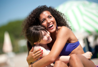 Two women in swimwear hug and smile on a sunny day at Camping Village Baia Blu La Tortuga in Sardinia, Italy.