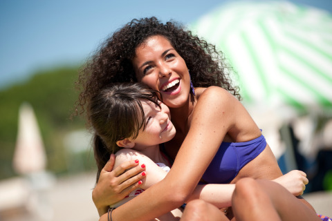 Two women in swimwear hug and smile on a sunny day at Camping Village Baia Blu La Tortuga in Sardinia, Italy.