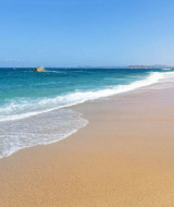 Playa de arena dorada con aguas turquesas y cielo azul cerca de Aglientu, Cerdeña, Italia, en un tranquilo día de verano.