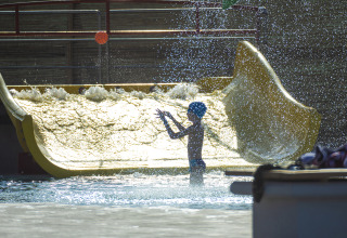 Bambino che gioca sotto gli spruzzi d’acqua allo scivolo al Camping Village Baia Blu La Tortuga, Sardegna.