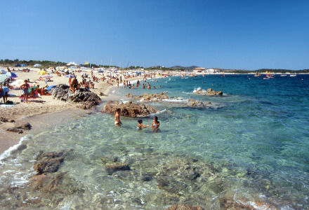 Playa cercana a Aglientu, Cerdeña, Italia, con aguas cristalinas y gente disfrutando del sol y del mar.