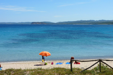 Smuk udsigt til stranden med klart blåt vand, en orange parasol og afslappende gæster i Sardinien, Italien.