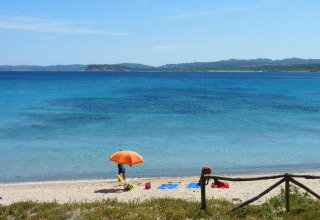 Smuk udsigt til stranden med klart blåt vand, en orange parasol og afslappende gæster i Sardinien, Italien.