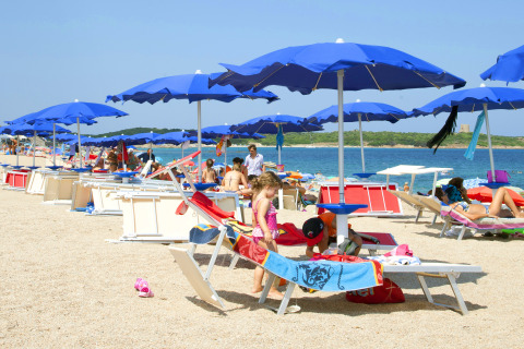 Children playing under blue umbrellas on the beach at Camping Village Baia Blu La Tortuga, Sardinia, Italy.