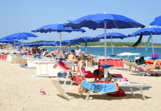 Children playing under blue umbrellas on the beach at Camping Village Baia Blu La Tortuga, Sardinia, Italy.
