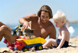 Un hombre y un niño juegan con camiones de juguete en la arena en Camping Village Baia Blu La Tortuga en Cerdeña.