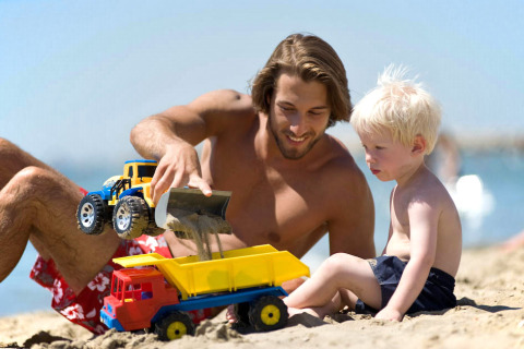 A man and a child play with toy trucks in the sand at Camping Village Baia Blu La Tortuga in Sardinia, Italy.