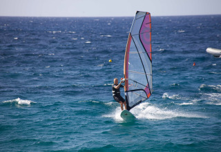 Person windsurfing on the blue sea at Camping Village Baia Blu La Tortuga holiday park in Sardinia, Italy.