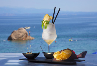 En forfriskende cocktail, chips og snacks serveret ved havet i Camping Village Baia Blu La Tortuga, Sardinien.