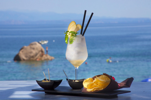 En forfriskende cocktail, chips og snacks serveret ved havet i Camping Village Baia Blu La Tortuga, Sardinien.