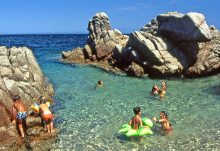 Niños juegan y nadan en agua clara entre rocas en Camping Village Baia Blu La Tortuga, Cerdeña, Italia.