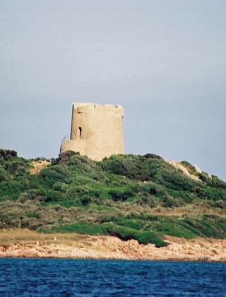 Torre antigua sobre una colina verde cerca de Aglientu, Cerdeña, fotografiada desde el mar azul cercano.