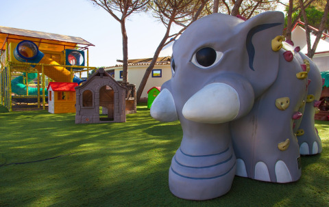 Legeplads med elefantskulptur, klatrevæg og legehuse ved Camping Village Baia Blu La Tortuga i Sardinien.