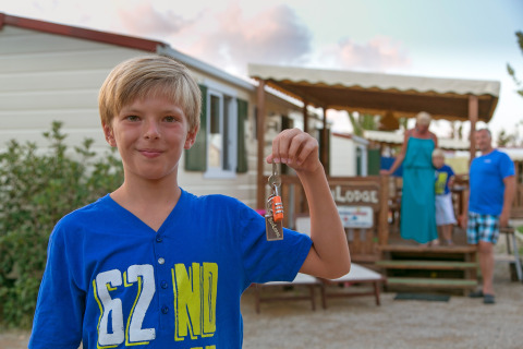 Niño sostiene una llave frente a SunLodge Redwood en el Camping Village Baia Blu La Tortuga en Italia.