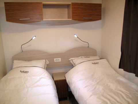 Dos camas individuales en SunLodge Redwood, Camping Village Baia Blu La Tortuga, Italia, con luz de lectura moderna.