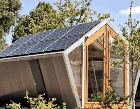 Duurzame Pentagon-lodge met zonnepanelen op het dak, grote ramen en veel groene bomen buiten.