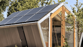Duurzame Pentagon-lodge met zonnepanelen op het dak, grote ramen en veel groene bomen buiten.