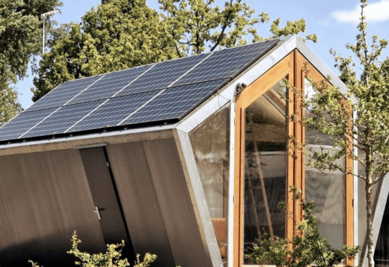 Duurzame Pentagon-lodge met zonnepanelen op het dak, grote ramen en veel groene bomen buiten.