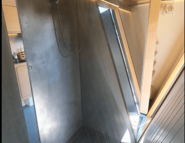 Ducha con paredes de concreto y ventana inclinada en la cabaña Pentagon de Buytenplaets Suydersee, Países Bajos.