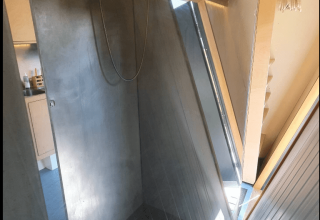 Doccia con pareti in cemento e finestra inclinata nella lodge Pentagon di Buytenplaets Suydersee, Paesi Bassi.