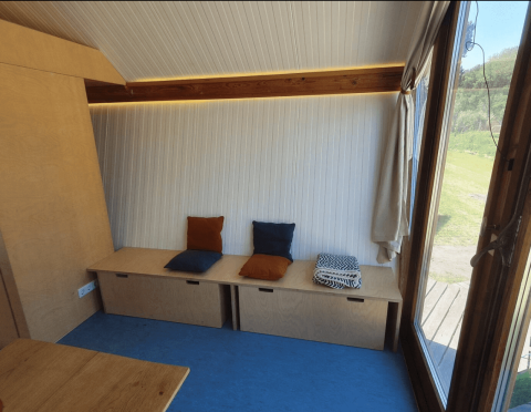 Acogedora cabaña Pentagon en Buytenplaets Suydersee con banco de madera, cojines y ventana exterior.