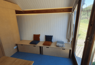 Lodge Pentagon à Buytenplaets Suydersee avec banc en bois, coussins colorés et grande fenêtre sur la nature.