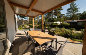 Terraza cubierta de una cabaña con mesa de comedor, seis sillas y vistas a otras cabañas rodeadas de árboles.