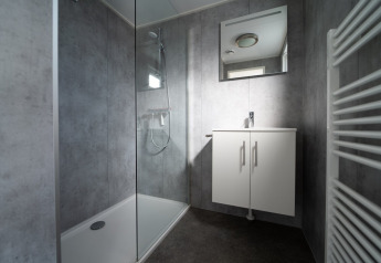 Salle de bain moderne de lodge avec douche vitrée, meuble lavabo et radiateur sèche-serviettes blanc.