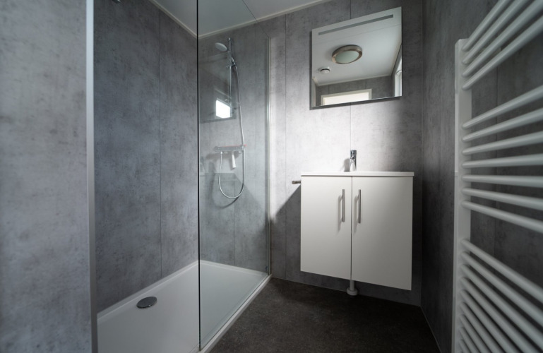 Baño moderno en lodge con ducha de cristal, lavabo con espejo y radiador toallero blanco.