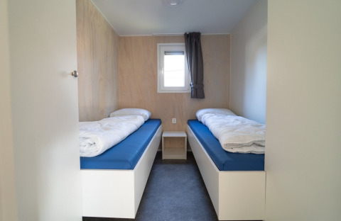 Dormitorio sencillo en una cabaña con dos camas individuales, colchones azules, edredones y ventana pequeña.