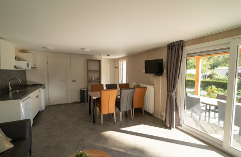 Indendørsbillede af en lodge med spiseområde, opholdsstue, køkken og udsigt til en overdækket terrasse.