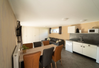 Interior luminoso y moderno de una cabaña con mesa de comedor, cocina equipada y cómodo sofá gris.
