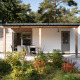 Moderne lodge med træfacade, terrasse og havemøbler, omgivet af grønne planter i en skov.