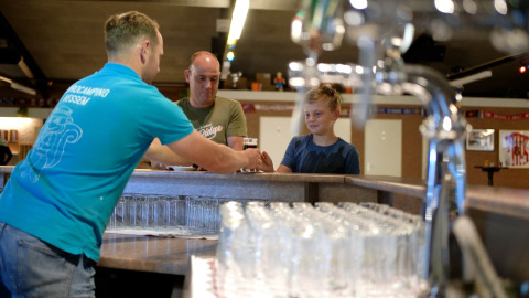 Barkeeper serviert einem Jungen und einem Mann ein Getränk in Eurocamping Vessem BV, Nordbrabant, Niederlande.