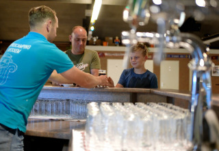 Bartender serves a drink to a boy and a man at the bar in Eurocamping Vessem BV, North Brabant, Netherlands.