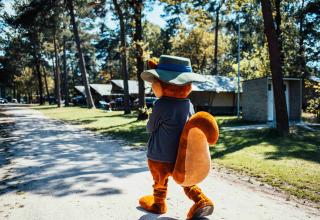 Maskot i egernkostume med hat går på en grusvej ved hytter i Eurocamping Vessem BV, Holland.