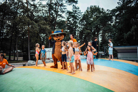 Kinder spielen mit einem Bärenmaskottchen auf einem Hüpfkissen im Eurocamping Vessem BV in Holland.