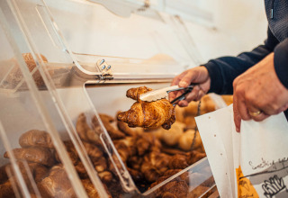 Iemand gebruikt een tang om een croissant uit een zelfbedieningsbak te nemen op een vakantiepark.