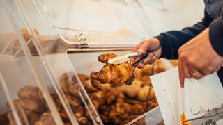 Persona usando pinzas para tomar un croissant de una vitrina de autoservicio en un parque vacacional.