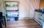 Zona de cocina en tienda safari del Camping Elbeling en Alemania, con estantería y utensilios.