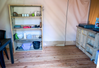 Area cucina in una tenda safari al Camping Elbeling in Germania con scaffale e utensili da cucina.