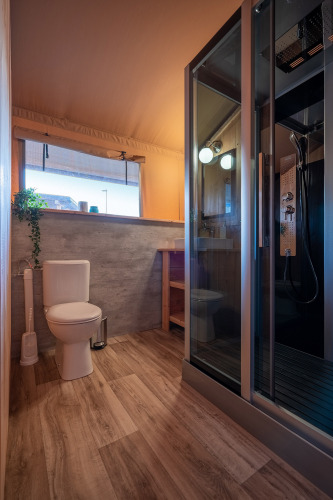 Baño moderno con suelo de madera, cabina de ducha y aseo en SunLodge Taiga, Camping Cisano/San Vito, Italia.