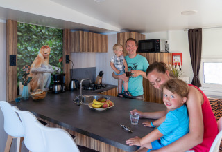 Familia en la cocina de la SunLodge Catalpa en Camping Cisano/San Vito, Italia, con un mural de mono en la pared.