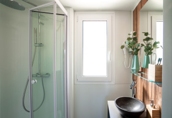 Modern bathroom at SunLodge Catalpa featuring a shower cabin, vessel sink and green vases by the mirror.