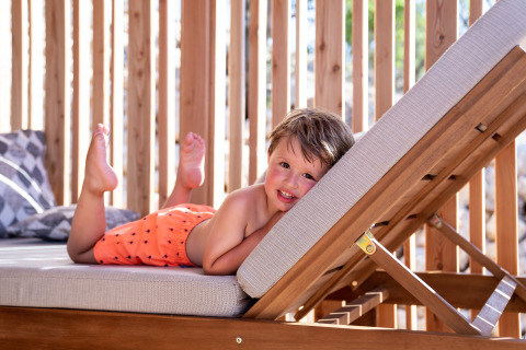 Enfant allongé sur une chaise longue en short de bain orange à SunLodge BigLeaf, Camping Cisano/San Vito, Italie.