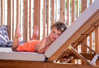 Niño relajándose en una tumbona con bañador naranja en SunLodge BigLeaf, Camping Cisano/San Vito, Italia.