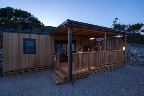 Vue du soir de SunLodge BigLeaf au Camping Cisano/San Vito, Italie, avec des personnes sur la terrasse en bois.