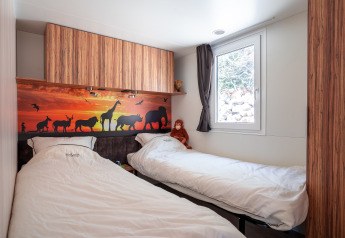 Kids' room with two single beds, animal-themed wall mural and window at SunLodge BigLeaf, Camping Cisano/San Vito, Italy.
