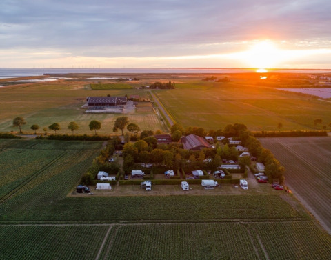 Atardecer en Camping 'de Val' en Zeeland, Países Bajos, con campos, caravanas y un paisaje tranquilo.